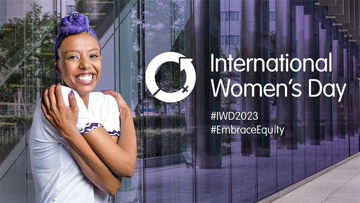 Woman with purple hair hugging herself next to the words "International Womens Day" with two hashtags used for the event - #IWD2023 and #EmbraceEquity